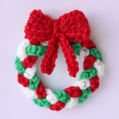 a crocheted christmas wreath with red, white and green ribbon hanging from it