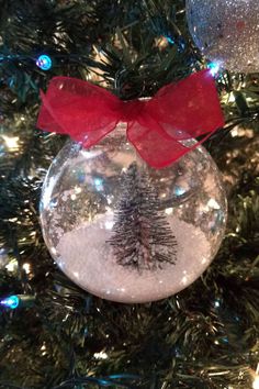 a snow globe ornament with a red bow hanging from the top on a christmas tree