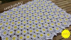 a crocheted blanket with yellow and white flowers on the bottom, sitting on a wooden table