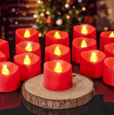 many red candles sitting on top of a table next to a christmas tree with lights in the background