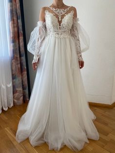 a woman wearing a white wedding dress with sheer sleeves