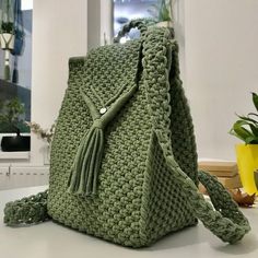 a green crocheted purse sitting on top of a table next to a potted plant