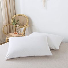 two white pillows sitting on top of a bed next to a chair with a plant in it