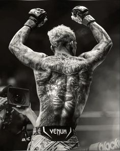 a man with tattoos on his back standing in front of a camera