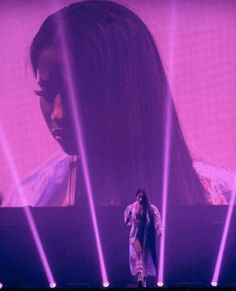 a woman standing on stage with lights behind her and an image of a man in the background