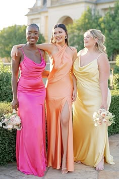 three beautiful women standing next to each other in long dresses with one holding her arm around the other's shoulder