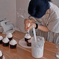 a woman is decorating cupcakes with icing on a table next to a blender