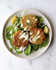 three crab cakes on a plate with spinach leaves and lemon wedges