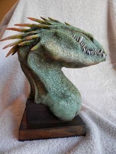 a statue of a green dragon with spikes on its head sitting on a wooden base