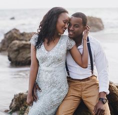 a man and woman are sitting on rocks by the ocean, smiling at each other