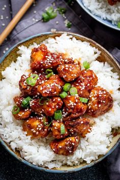 two bowls filled with rice and chicken on top of a blue table cloth next to chopsticks