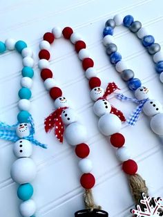 three snowman beads are attached to necklaces on a white table with red, white and blue decorations