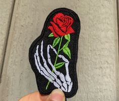 a hand holding a patch with a red rose on it and a skeleton's arm