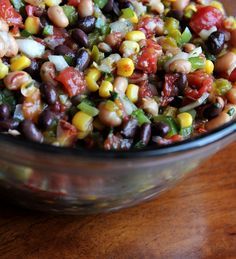 a glass bowl filled with black beans, corn and tomato salad on top of a wooden table