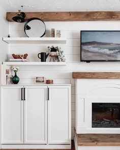 a living room with white walls and wooden shelves on the wall, along with a flat screen tv mounted above a fireplace