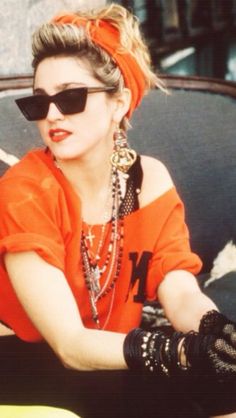 a woman in an orange shirt and black gloves sitting on a bench with her hand resting on the arm