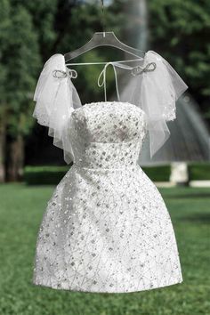 a wedding dress hanging on a hanger in front of a park with trees and grass