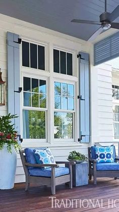 a porch with two chairs and a ceiling fan on the side of it, next to a large potted plant