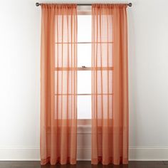 an orange sheer curtain hanging on the side of a window in front of a white wall