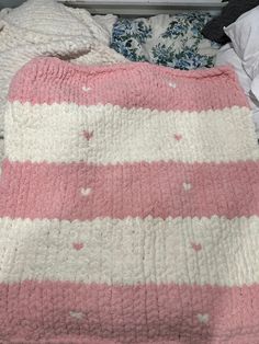 a pink and white blanket sitting on top of a bed next to two pillow cases