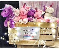 several stuffed animals in a wooden crate with lights around them and a sign that says adopt a unicorn