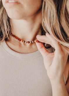 a woman wearing a necklace with beads on it's neck and holding her hands to her chest