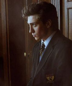 a young man in a suit and tie looking out the window with his hands on his hips