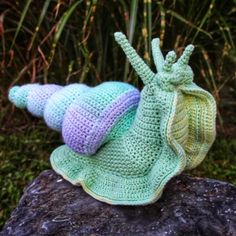 two crocheted snail hats sitting on top of a rock next to some grass