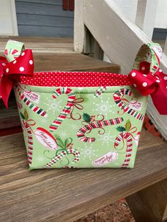 a green christmas treat bag with red bows and candy canes on the side sitting on a wooden bench