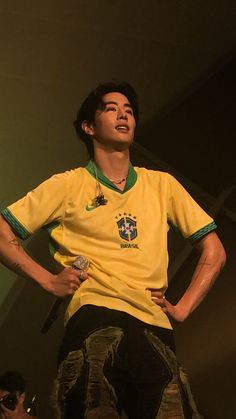 a young man standing on top of a wooden platform wearing a yellow shirt and black pants