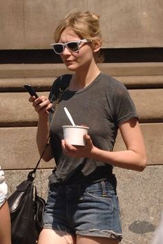 a woman is holding a cup and looking at her cell phone while walking down the street