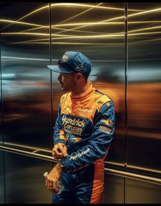 a man standing in front of a glass wall with his hand on his hip and wearing a hat