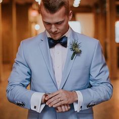 a man in a blue suit and bow tie is looking down at his wedding ring