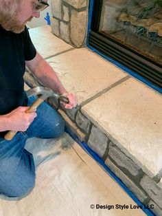 a man sitting on the ground working on a stone fireplace with a pair of hammers