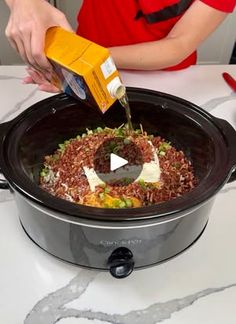 a person pouring dressing into a crock pot filled with rice, beans and vegetables