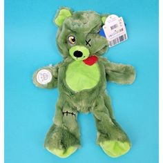 a green teddy bear with a tag on it's ear and eyes, sitting against a blue background