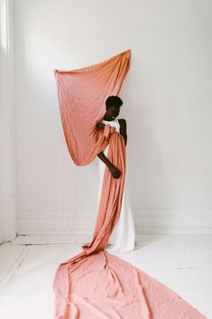 a woman with an orange shawl draped over her head, standing in front of a white wall