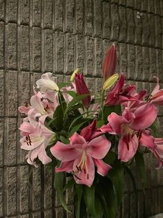 a vase filled with pink and white flowers next to a brick wall on the side of a building