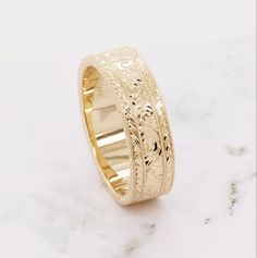 a gold wedding ring with intricate engraving on it's sides, sitting on a marble surface