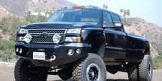 a large black truck parked on top of a dirt covered field with mountains in the background