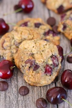 cookies with cherries and chocolate chips are on a wooden surface, surrounded by fresh cherries