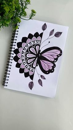 a drawing of a butterfly on top of a spiral notebook next to a potted plant