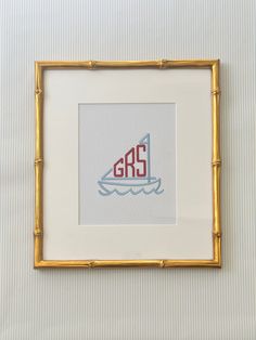 a cross - stitch sailboat is framed in a gold frame