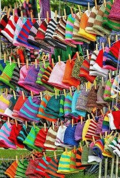 colorful knitted hats and sweaters hanging on clothes pins in the grass at an outdoor market