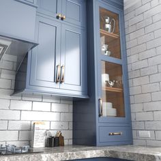 a kitchen with blue cabinets and marble counter tops in front of a white brick wall