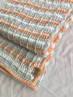 two crocheted blankets sitting on top of a bed covered in white and orange