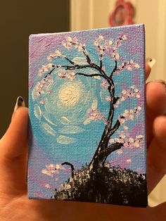 a person holding up a small painting with flowers on it and a tree in the background