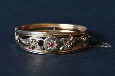 An ornate 9 carat gold, Edwardian bangle with what looks to be a star and thistle pattern. It has seen some wear and has taken some knocks (with dings) as a result but is still completely intact with no missing pieces or stones (please refer to images). There are a total of three small rubies with the largest being surrounded by a single row of diamond chips.  One of our favourite features lies in the detailing where you can see very small millegrain patterns applied around the entire bangle. Th Antique Yellow Gold Bangle For Formal Occasions, Victorian Gold Bangle Bracelet For Formal Events, Victorian Gold Bracelet For Formal Occasions, Victorian Style Yellow Gold Bracelets With Intricate Design, Victorian 14k Gold Bangle For Formal Occasions, Heirloom Gold Bracelet Hallmarked, Victorian Bangle Bracelets For Formal Occasions, Victorian Bracelets With Intricate Design For Formal Occasions, Ornate Gold Bangle Bracelet For Formal Occasions