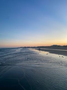 the sun is setting at the beach with people walking in the water and on the sand