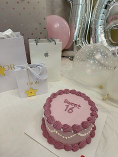 a pink birthday cake sitting on top of a table next to balloons and gift bags